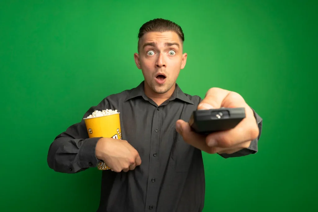 Homme surpris par la qualité de son IPTV sans coupure VraiTV, télécommande en main et popcorn prêt